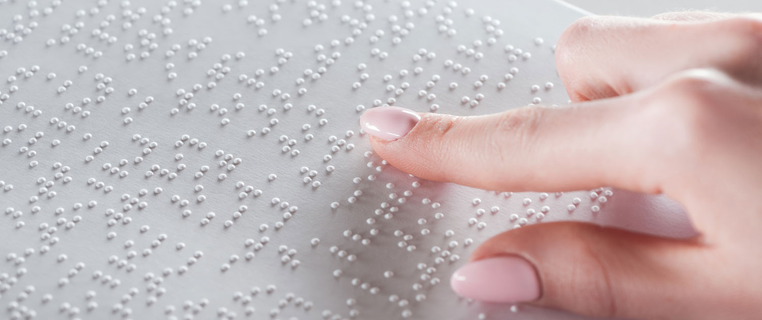 A woman's right hand touches different letters on a metal plate containing the Braille alphabet. Blind people can read texts using Braille.