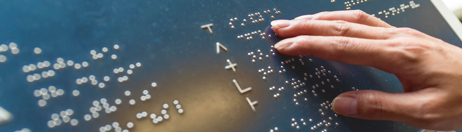 A woman's right hand touches different letters on a metal plate containing letters in the Braille alphabet. Blind people can read texts using Braille characters.