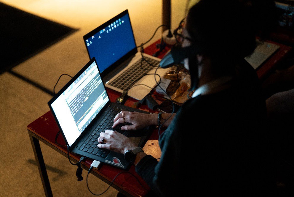 A professional speech-to-text interpreter working on her laptop. She is using respeaking, a shorthand mask, and her keyboard. The interpreted live text appears on her screen. To the right, a second laptop is visible. The second speech-to-text interpreter works on this one. © https://www.beat-the-silence.at/