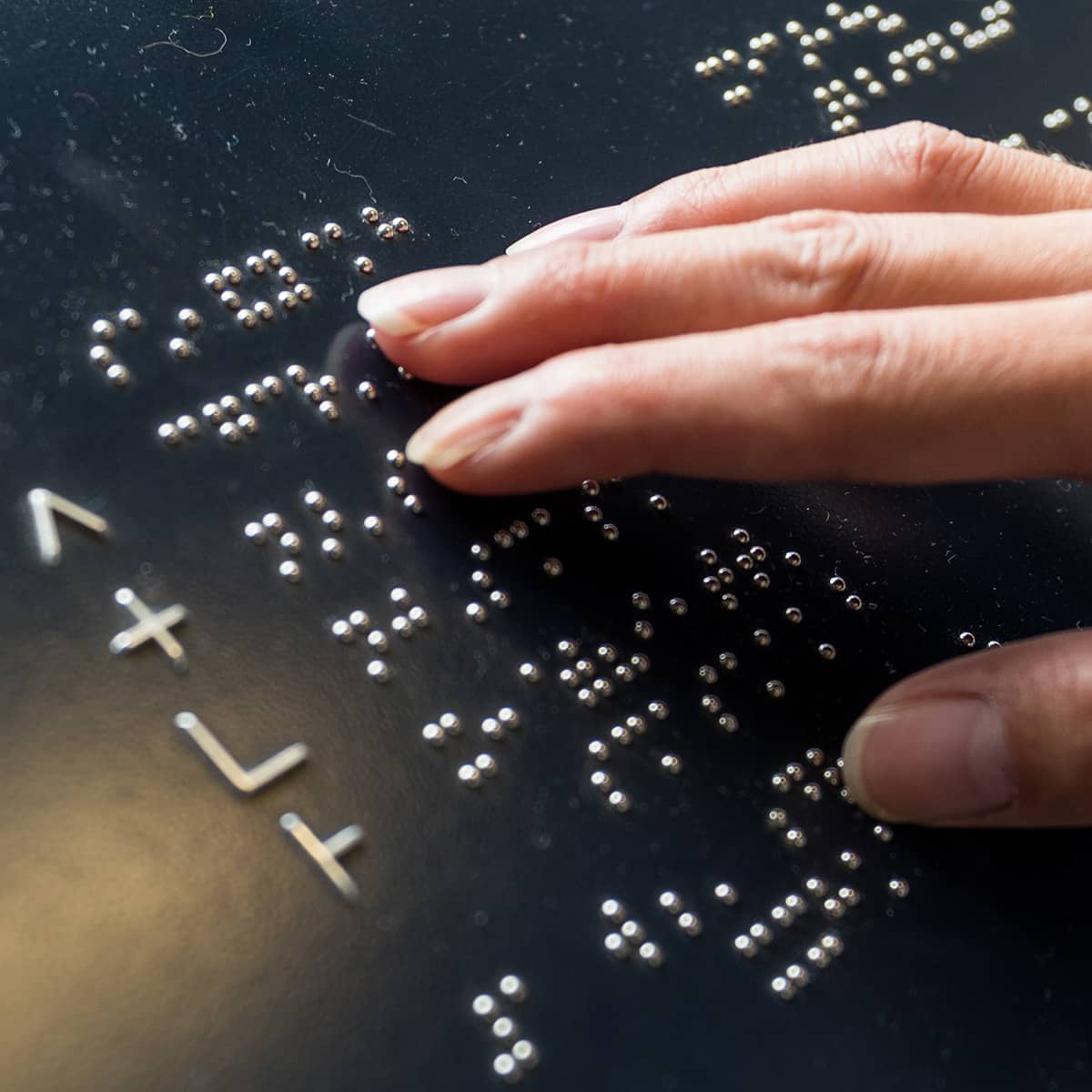 A woman's right hand touches different letters on a metal plate containing the letters of the Braille alphabet. Blind people can read texts using Braille characters.