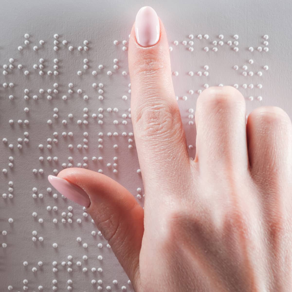 A woman's right hand touches different letters on a metal plate. The letters are in the Braille alphabet. Blind people can read texts using Braille.